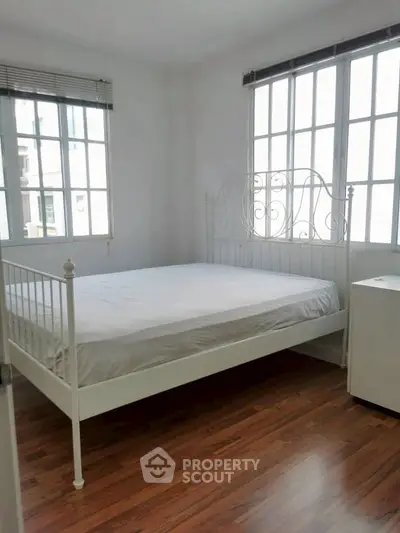 Bright bedroom with large windows and elegant metal bed frame, featuring hardwood floors.
