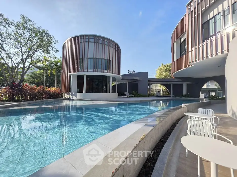 Luxurious modern building with stunning pool and outdoor seating area under clear blue sky.