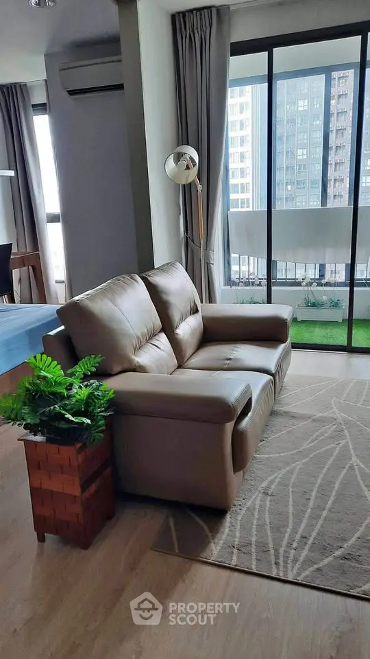 Modern living room with leather sofa and large windows overlooking cityscape.