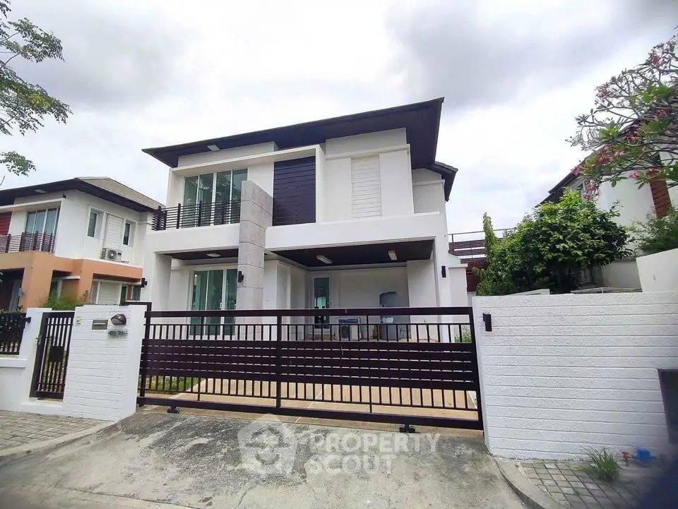 Modern two-story house with sleek design and gated entrance in a suburban neighborhood.