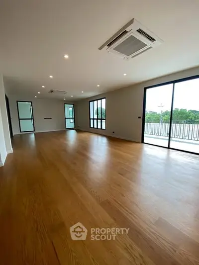 Spacious modern living room with wooden flooring and large windows opening to a balcony.