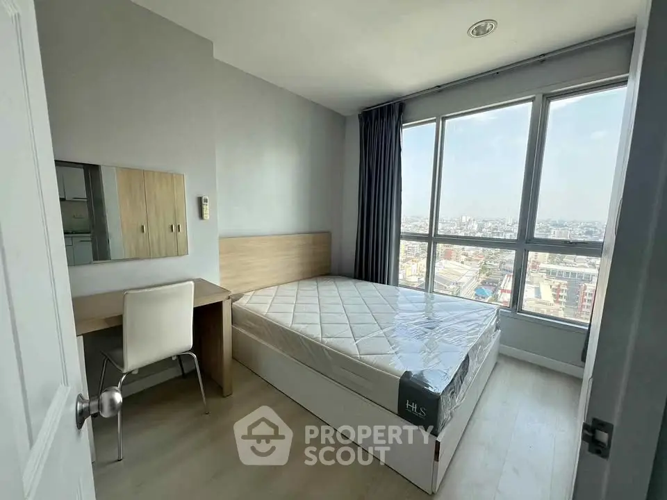 Modern bedroom with large windows and city view, featuring a bed and study desk.