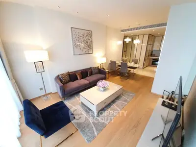 Elegant living room with modern decor and open dining area, featuring stylish furniture and warm lighting.