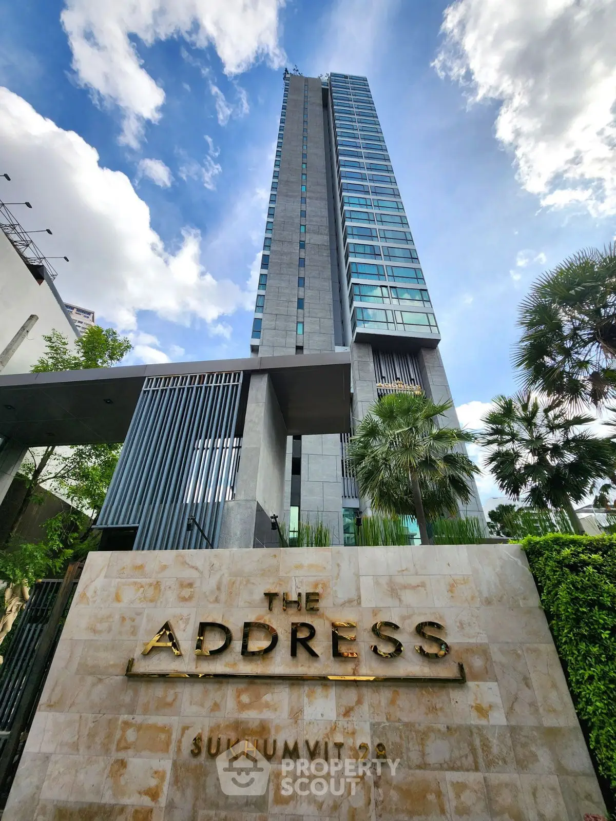 Luxurious high-rise building with modern design at The Address Sukhumvit 28, surrounded by lush greenery.