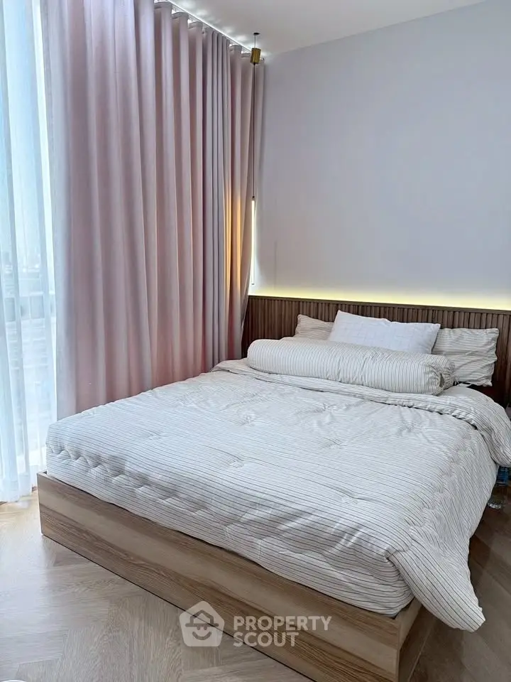 Elegant bedroom with soft pink curtains and modern lighting, featuring a cozy bed with plush pillows.