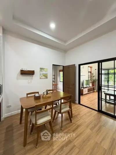 Modern dining area with wooden table and chairs, adjacent to a cozy living room with natural light.