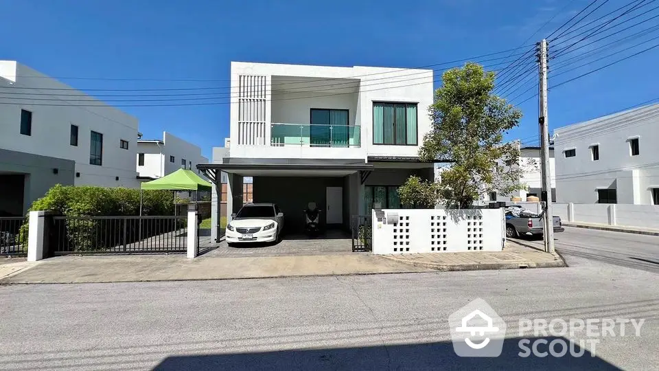 Modern two-story house with carport and lush greenery in a serene neighborhood.