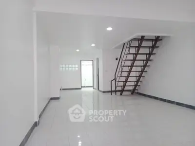 Spacious open-plan interior with sleek staircase and modern white tile flooring.