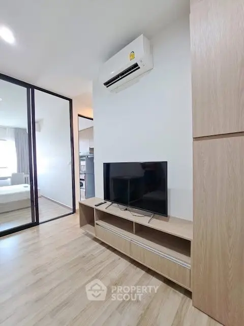 Modern living room with sleek wooden flooring and air conditioning, featuring a TV and stylish cabinetry.