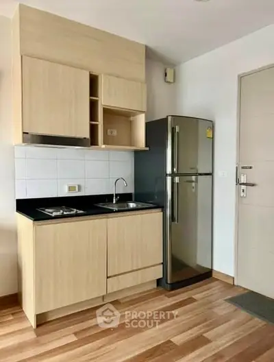 Modern compact kitchen with sleek cabinets and stainless steel fridge in a stylish apartment.