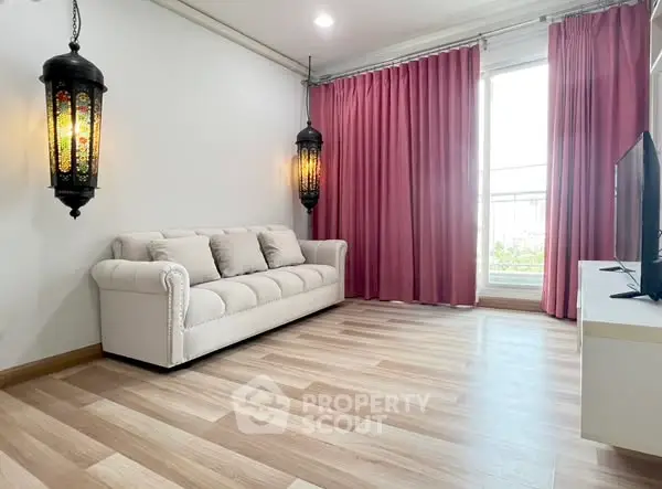 Elegant living room with stylish lanterns and pink curtains, featuring a cozy white sofa and modern TV setup.