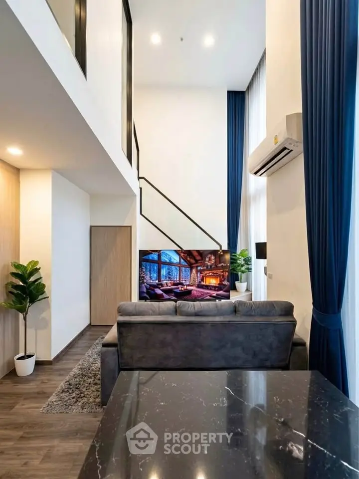 Modern living room with high ceilings and stylish decor, featuring a cozy sofa and large TV.