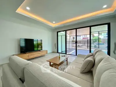 Spacious living room with modern sofa and large TV, featuring sliding glass doors to outdoor area.