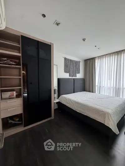 Modern bedroom with sleek black wardrobe and large window for natural light.