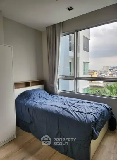 Cozy bedroom with large window offering city view, featuring a single bed and modern decor.