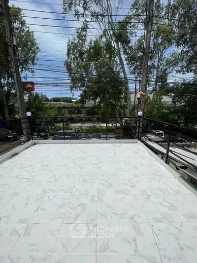 Spacious balcony with tiled flooring and scenic view of lush greenery and street below.