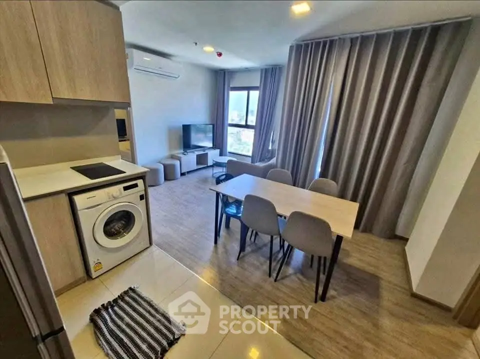 Modern open-plan living room with kitchen and dining area, featuring a washing machine and stylish decor.