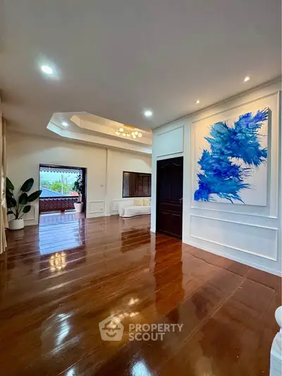 Spacious living room with polished wooden floors and modern art, leading to a large balcony with scenic views.