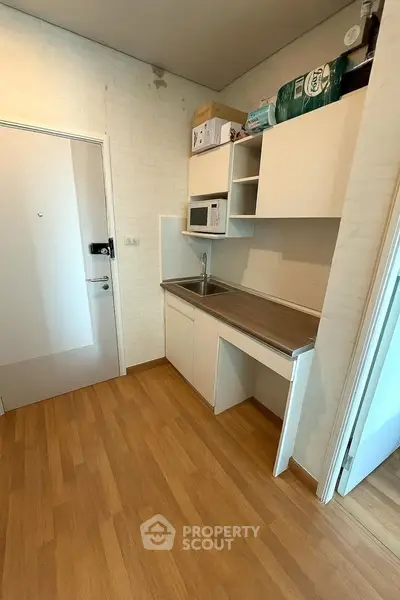 Compact kitchen with wooden flooring and white cabinetry, featuring a microwave and sink.
