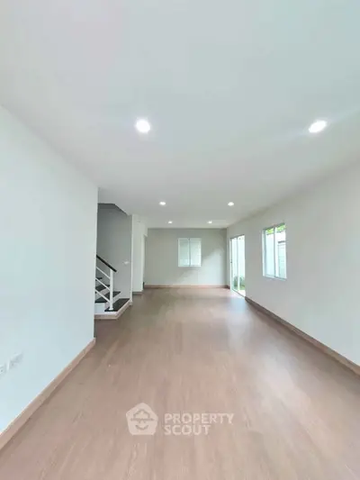 Spacious open-plan living room with wooden flooring and modern lighting, perfect for family gatherings.