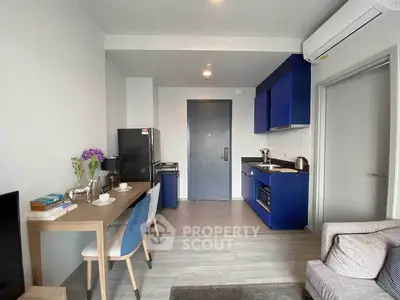 Modern apartment interior with open kitchen and cozy living area, featuring stylish blue cabinetry and dining setup.