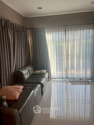 Cozy living room with leather sofa and large window draped with curtains