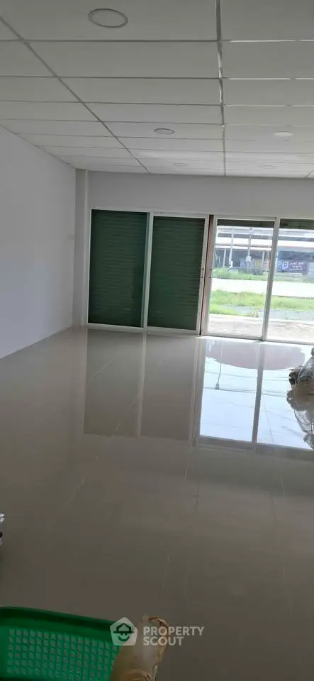 Spacious empty room with glossy tiled floor and large windows offering natural light.