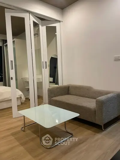 Modern compact living room with glass table and sliding doors to bedroom