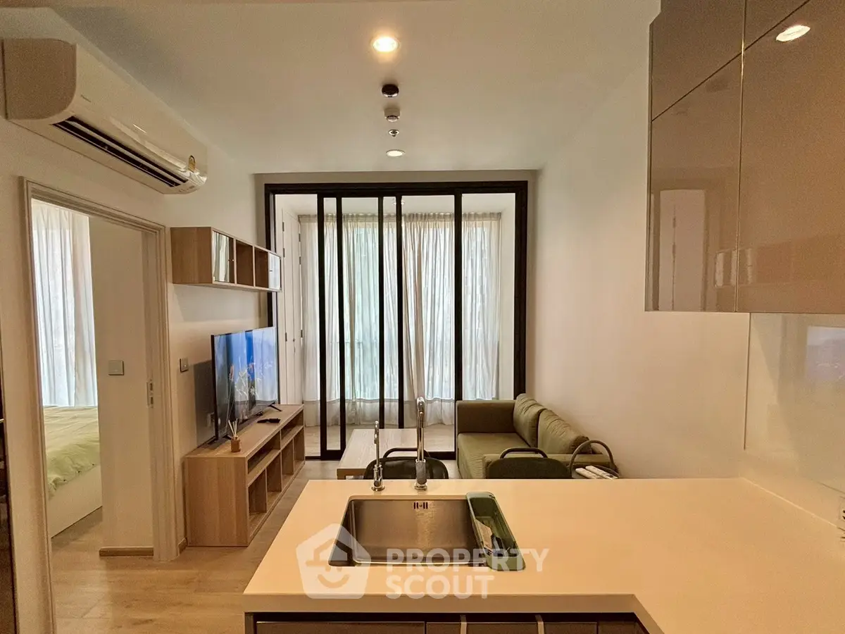 Modern open-layout living room with kitchen, featuring sleek design and natural light from large windows.