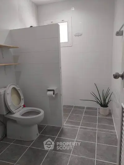 Modern bathroom with tiled floor, white walls, and a potted plant, featuring a toilet and open shelving.