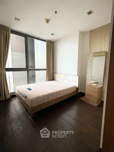 Spacious bedroom with large window and modern furnishings in a high-rise apartment.