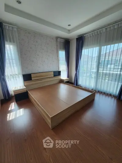 Spacious bedroom with elegant wooden flooring and large windows for natural light.