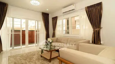 Elegant living room with beige sofa, glass coffee table, and large windows with brown curtains.