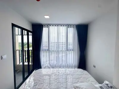 Bright bedroom with large window and balcony access, featuring modern curtains and a comfortable bed.