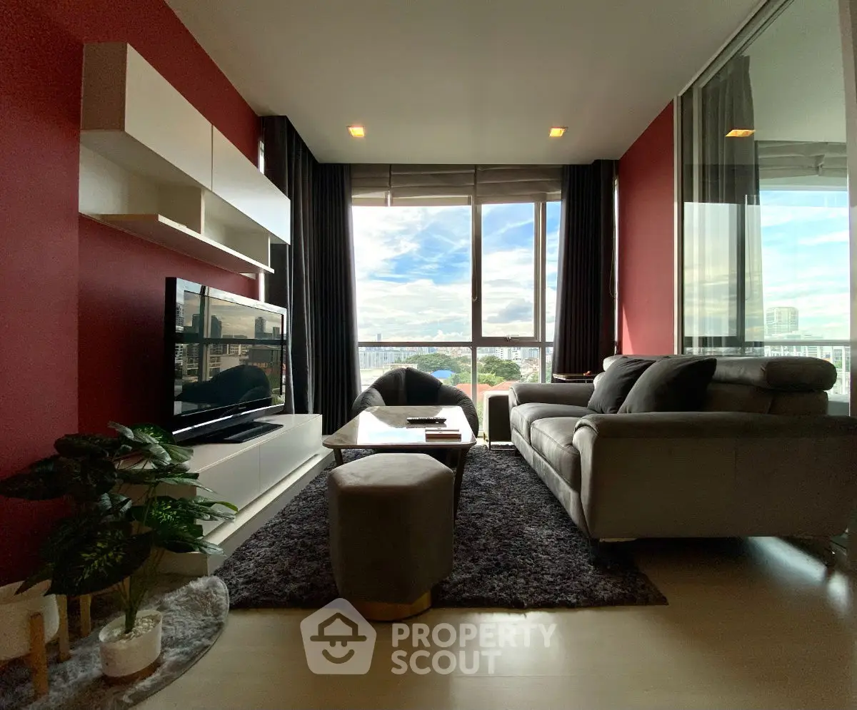 Modern living room with large window and city view, featuring stylish furniture and vibrant red walls.