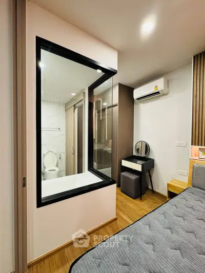 Modern bedroom with glass partition to bathroom, featuring sleek design and wooden flooring.