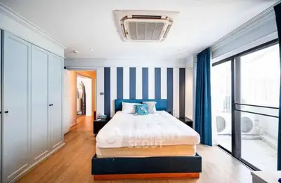 Spacious modern bedroom with striped accent wall and large window for natural light.