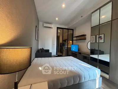 Modern bedroom with stylish decor, featuring a cozy bed, mirrored wardrobe, and a glimpse of a compact kitchen.