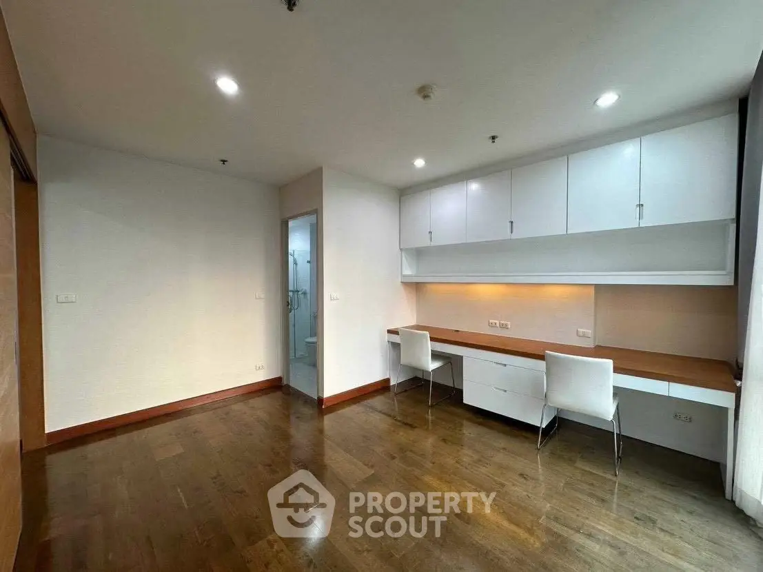 Spacious study room with built-in desk and cabinets, featuring elegant wooden flooring and modern lighting.