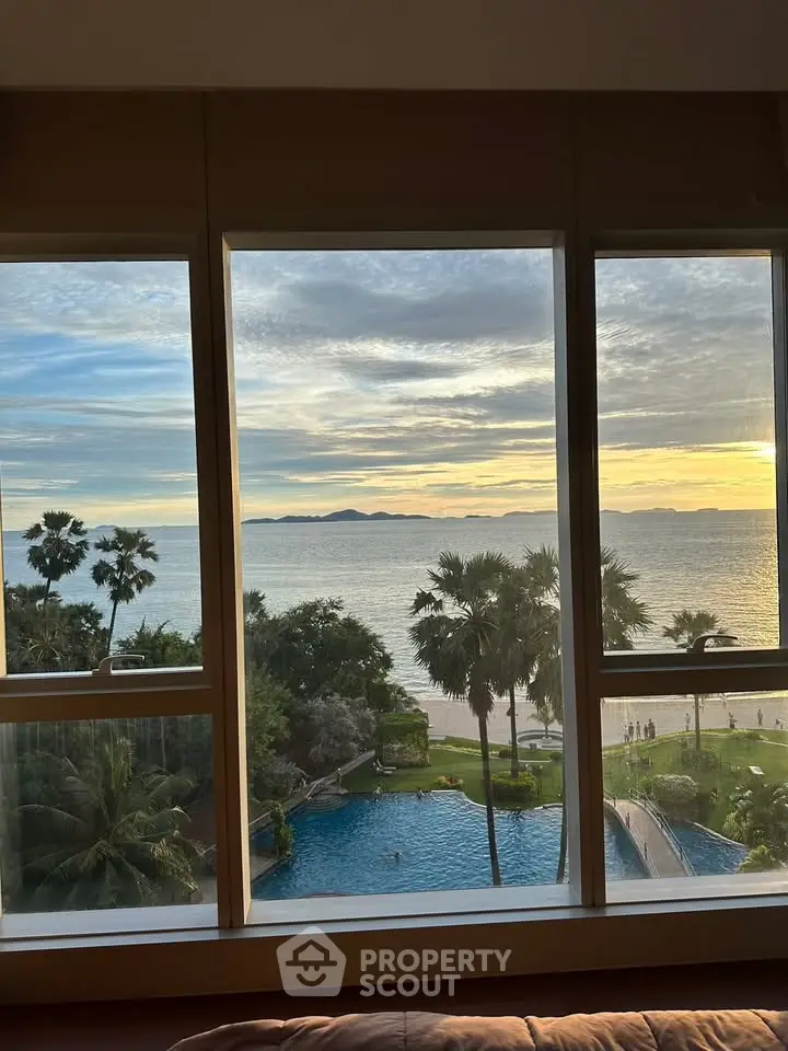 Stunning ocean view from a high-rise apartment window overlooking a pool and palm trees at sunset.