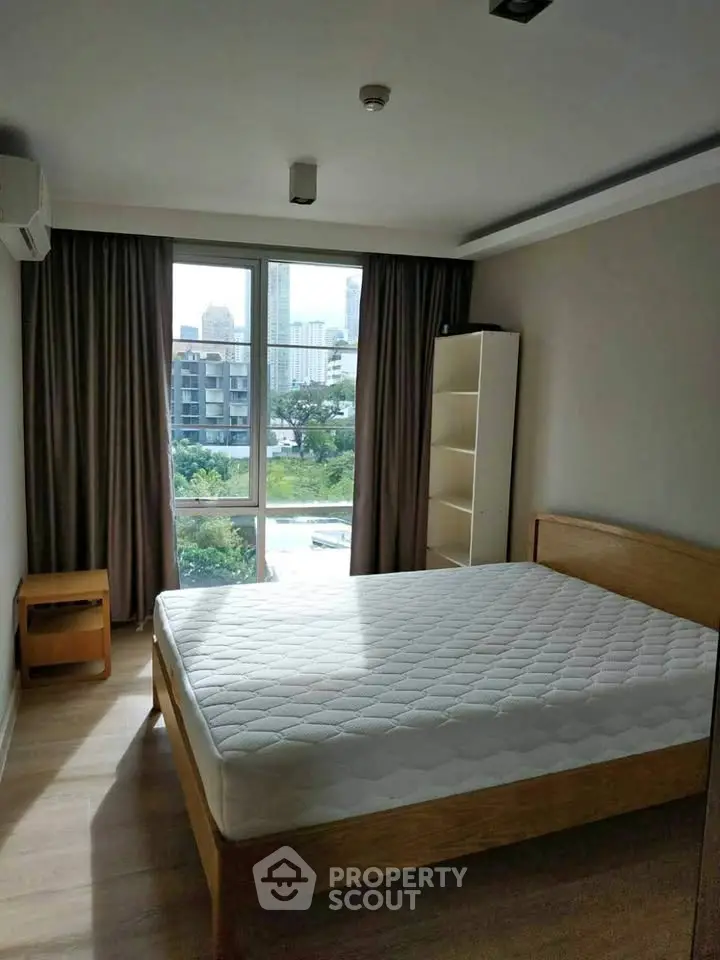 Spacious bedroom with large window offering city view, featuring a comfortable bed and modern furnishings.