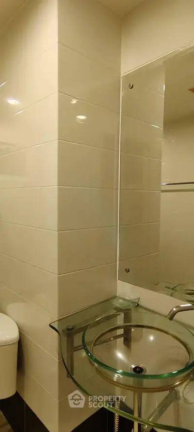 Modern bathroom with glass sink and white tiled walls, showcasing sleek and contemporary design.