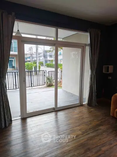 Spacious living room with sliding glass doors leading to a balcony, featuring elegant curtains and wooden flooring.