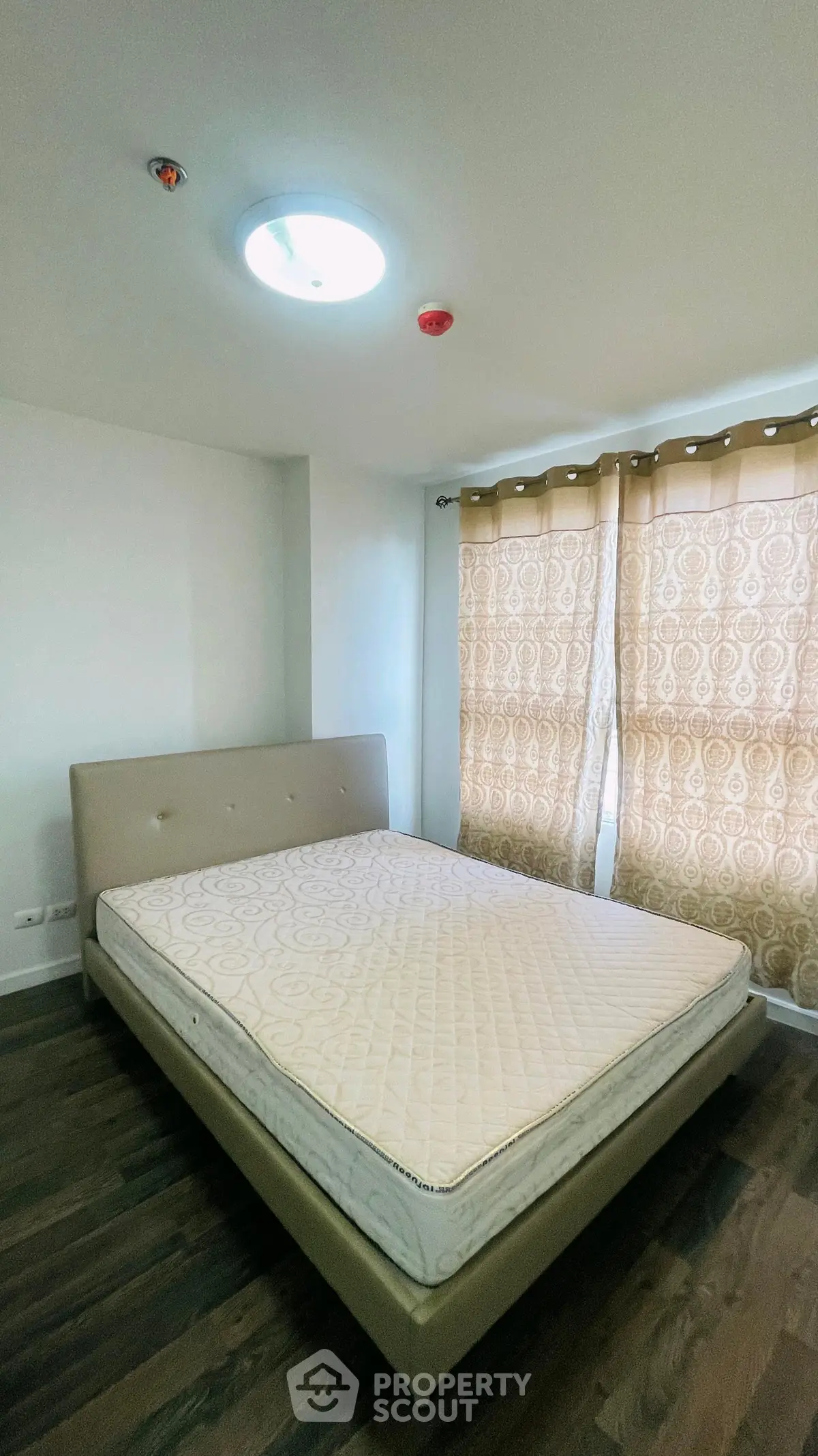 Spacious bedroom with elegant bed and natural light through patterned curtains.