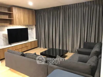 Modern living room with sleek gray sofa and large TV, featuring elegant wooden accents and floor-to-ceiling curtains.