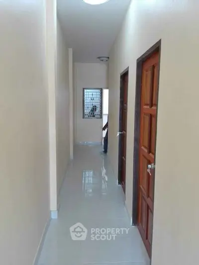 Bright hallway with polished tile flooring and wooden doors, leading to a window with a view of the outdoors.