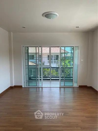 Spacious and well-lit living room with polished hardwood floors and large glass doors leading to a charming balcony, perfect for modern living.
