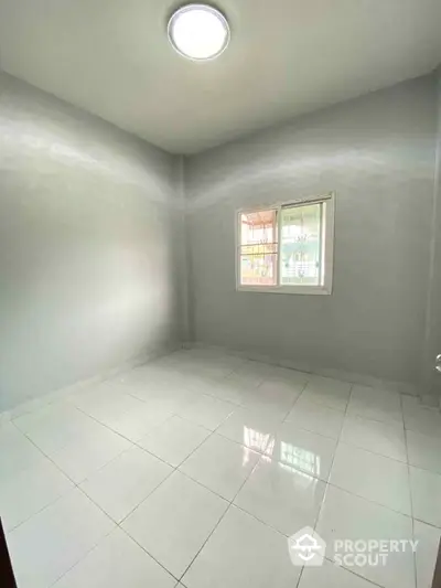 Spacious empty room with white tiled flooring and a window, perfect for customization and personal design.