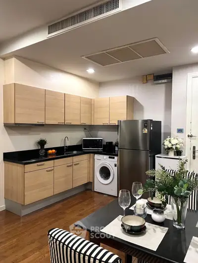 Modern kitchen with wooden cabinets, stainless steel fridge, and dining area with elegant table setting.