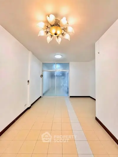 Spacious empty room with elegant chandelier and tiled flooring, perfect for customization.